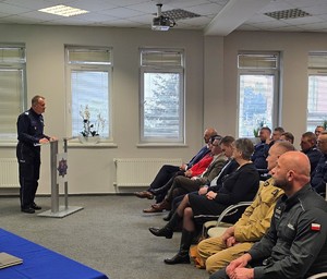 Przy pulpicie stoi Komendant Wojewódzki Policji w Krakowie nadinsp. Artur Bednarek, po prawej stronie siedzą zaproszeni goście wraz z przedstawicielami służb, Służba Więzienna, Straż Pożarna, za nimi funkcjonariusze Komendy Powiatowej Policji w Chrzanowie.