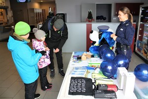 Policjantka stoi przy stoisku, naprzeciw niej dwójka dzieci z rodzicem.