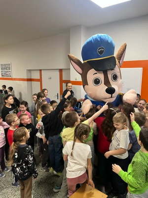 Dzieci stojące na korytarzy szkoły i maskotka.