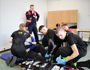 Uczestnicy jednocześnie udzielają pomocy osobie poszkodowanej, używając sprzętu medycznego.