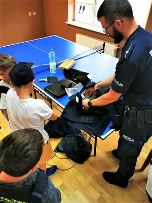 Policjant prezentuje dzieciom elementy wyposażenia wykorzystywanego podczas służby.