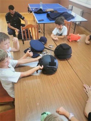Policjant prezentuje dzieciom policyjne nakrycia głowy i opowiada o wyposażeniu funkcjonariuszy.