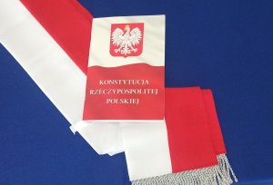Konstytucja na tle niebieskiego płótna oraz biało czerwonej szarfy