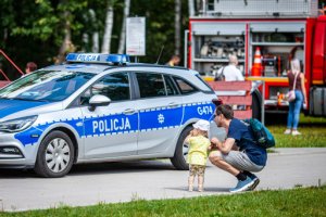 Oznakowany radiowóz , na który wpatruje się małoletnie dziecko z opiekunem