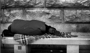 Na załączonej czarno - białej fotografii widoczny jest mężczyzna , który śpi na betonowej ławce.
Po leżącym mężczyzną rozłożony jest koc.